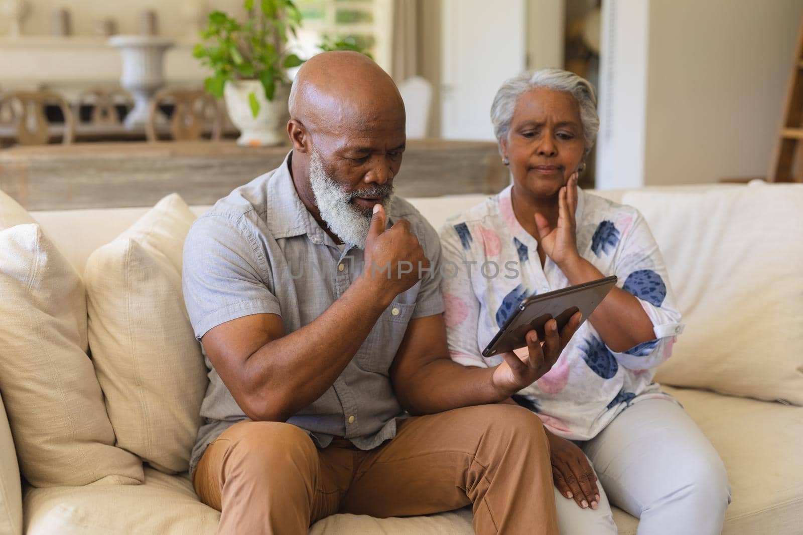 Senior african american couple sitting on sofa using tablet. retreat, retirement and happy senior lifestyle concept.