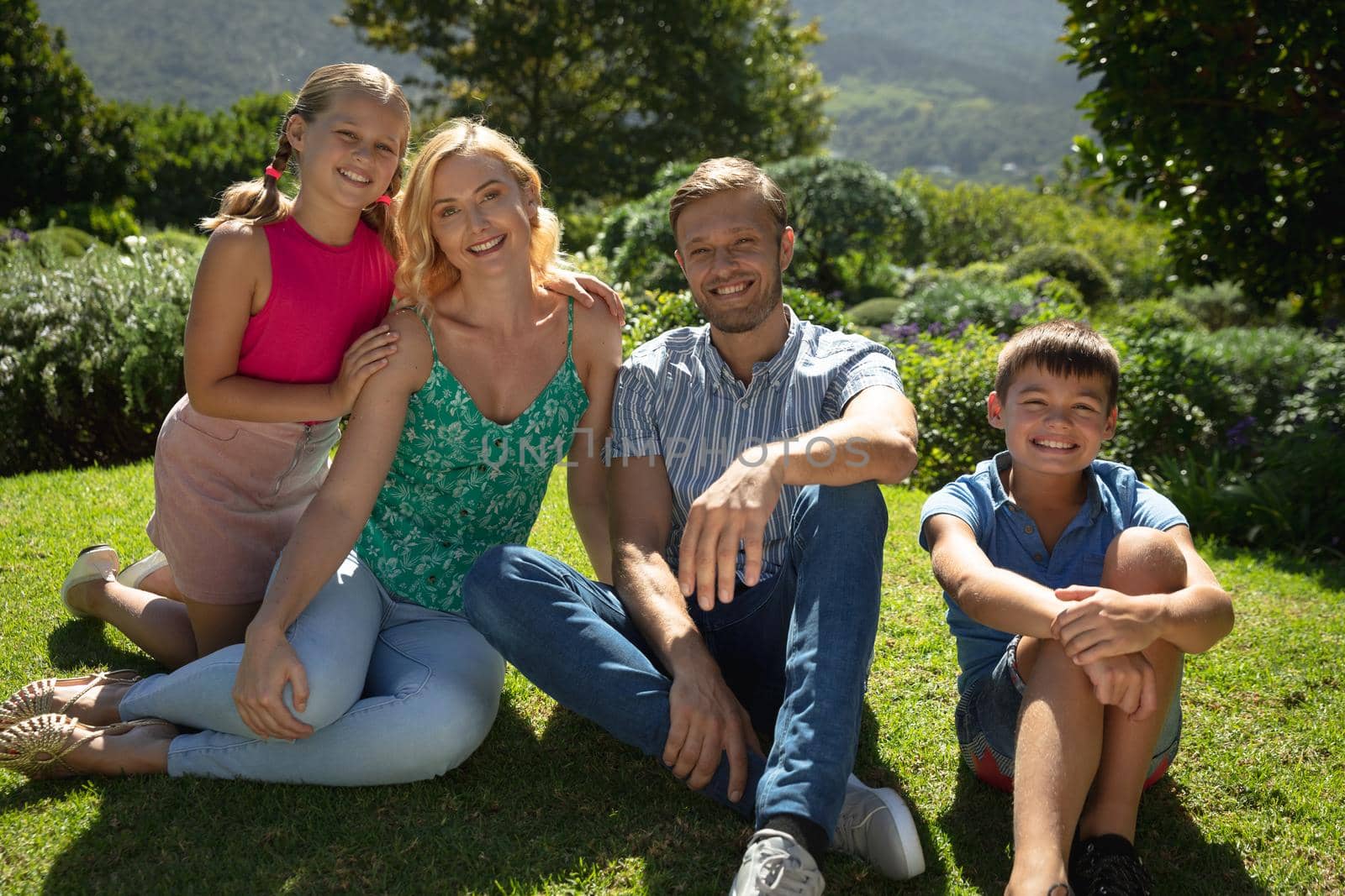 Portrait of happy caucasian couple with daughter and son outdoors, sitting in sunny garden. family enjoying quality free time together.