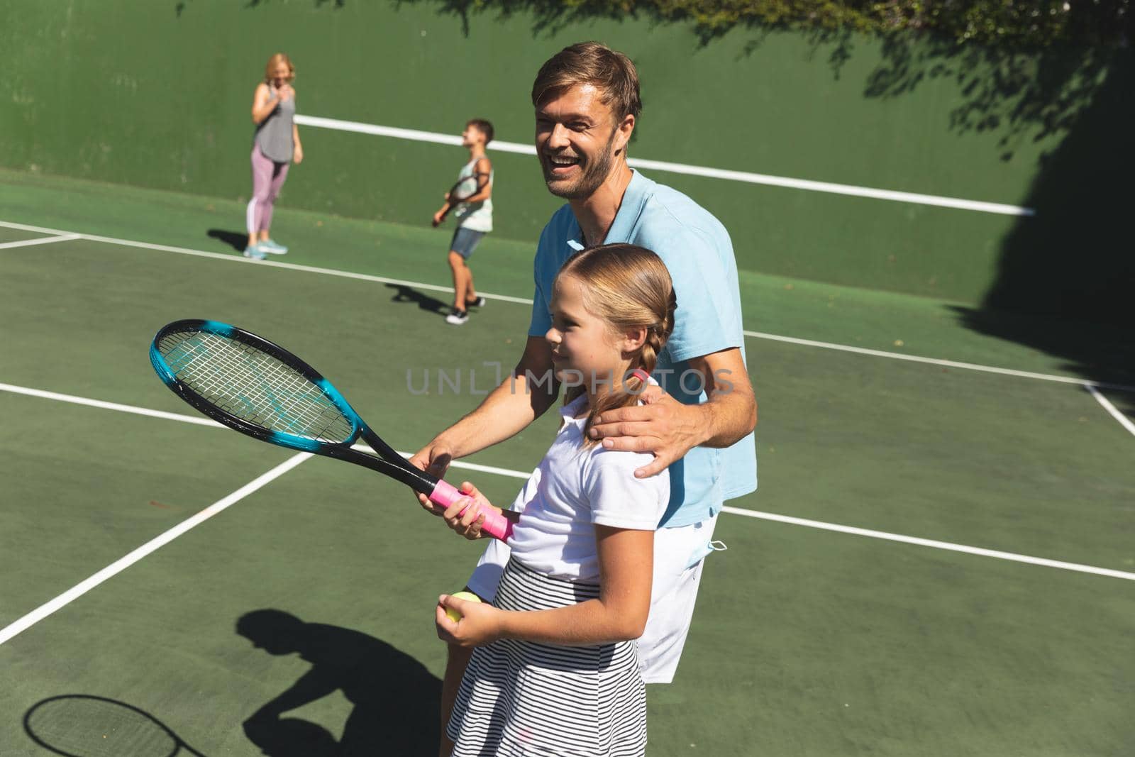 Happy caucasian couple with daughter and son outdoors, playing tennis on tennis court. family enjoying healthy free time activities together.