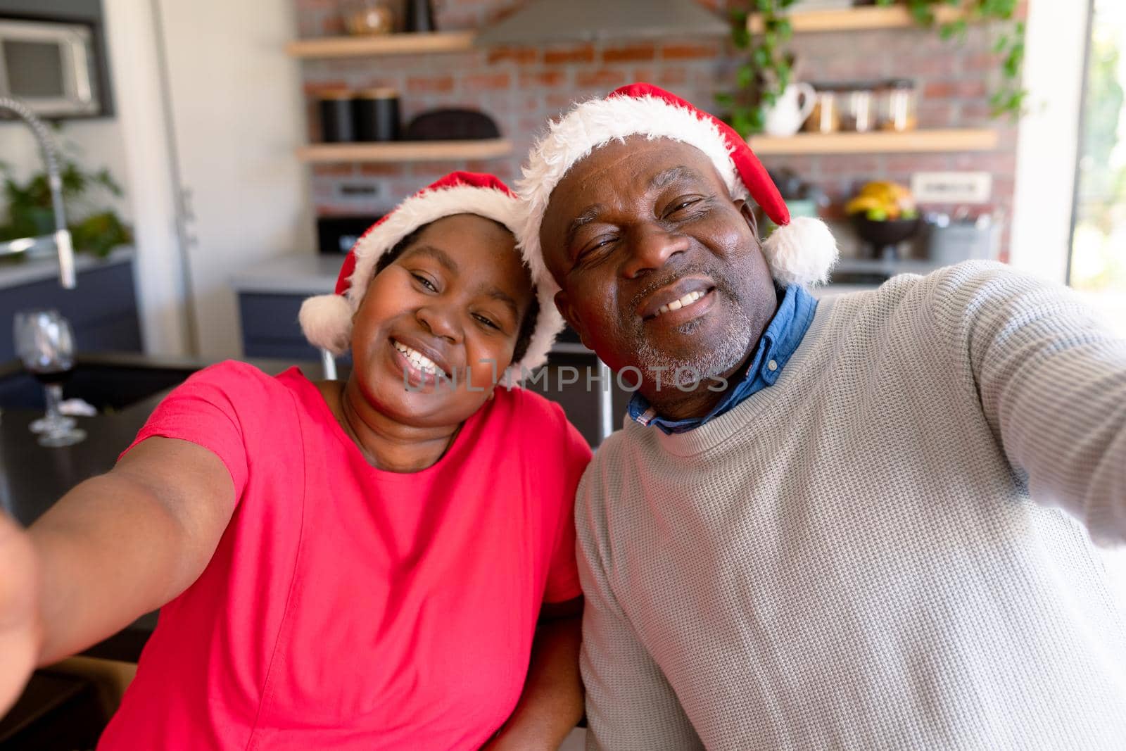 Happy african american senior couple taking selfie in kitchen at christmas time. retirement lifestyle, christmas festivities and communication technology.