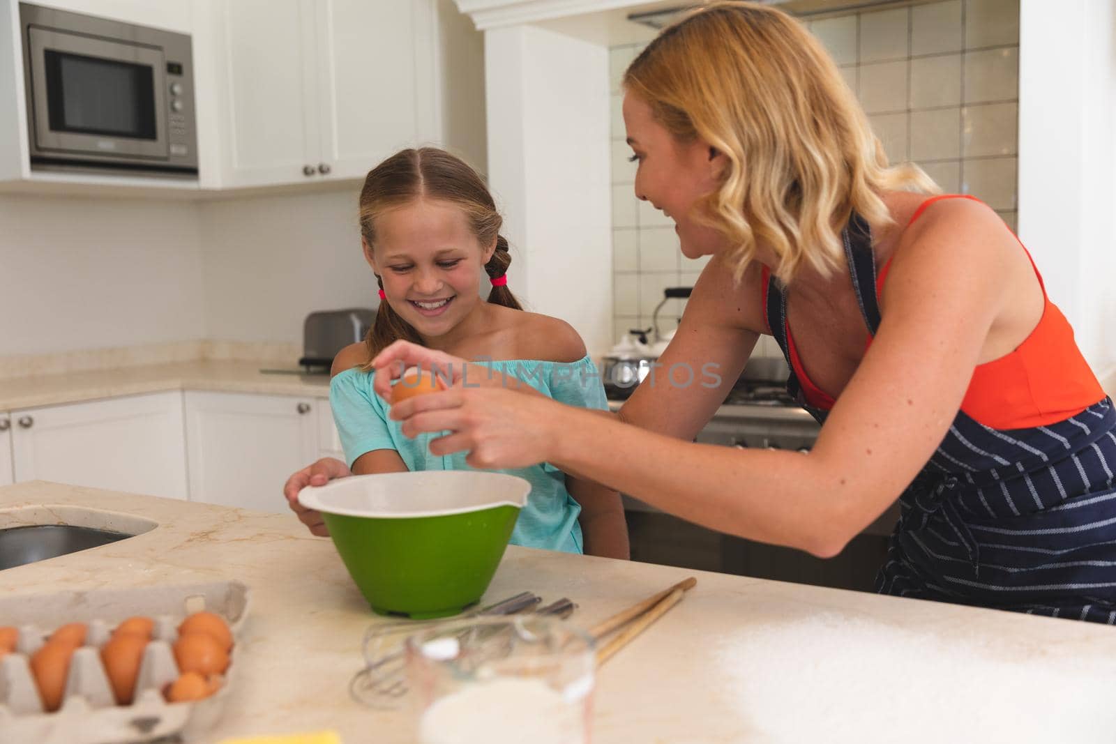 Caucasian mother and daughter baking and smiling in kitchen. family enjoying quality free time preparing food together.