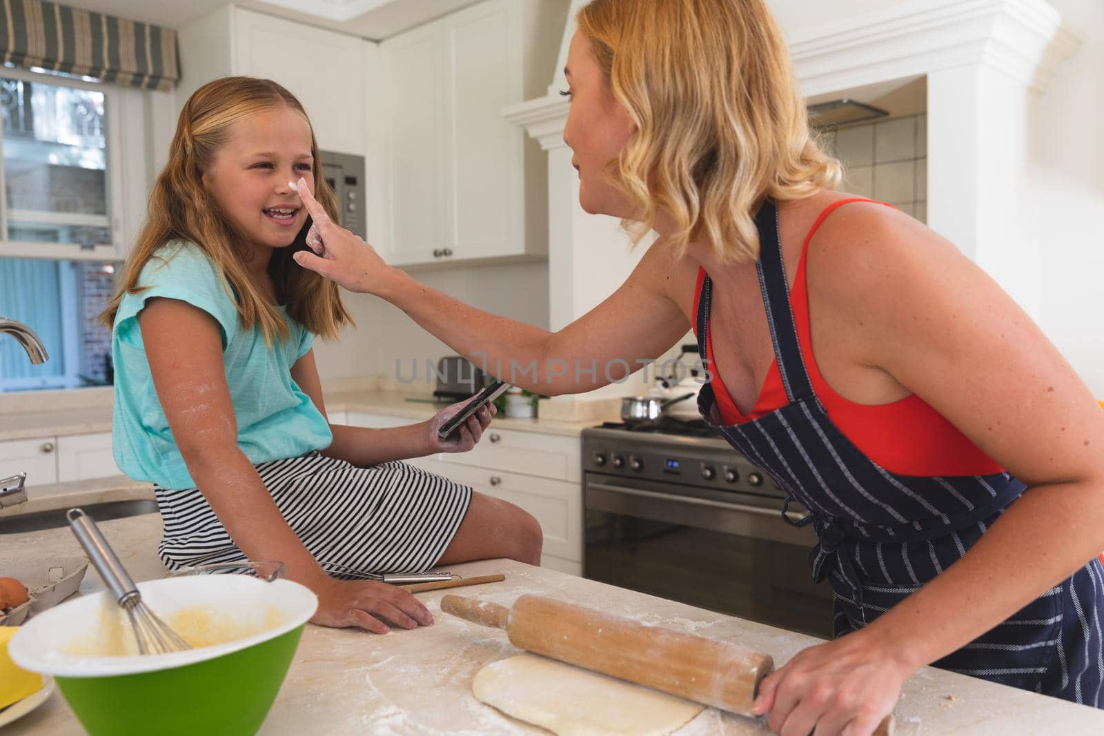 Happy caucasian mother and daughter having fun baking in kitchen. family enjoying quality free time preparing food together.