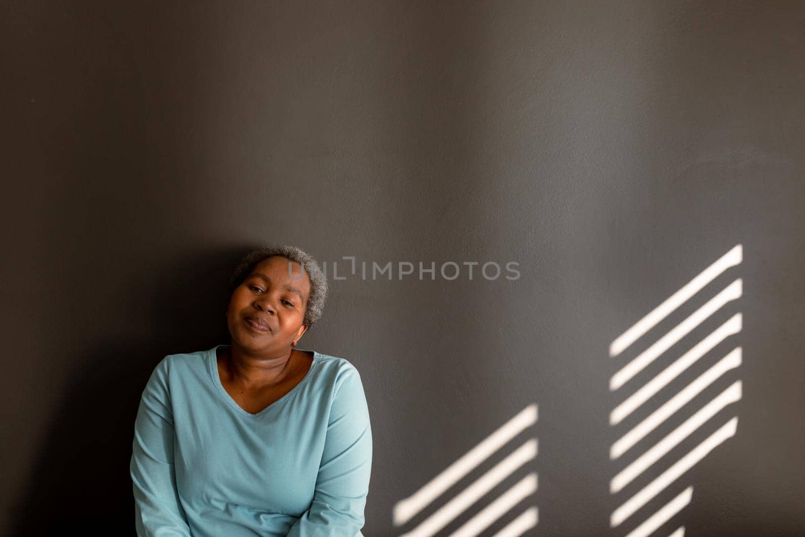 Relaxed african american senior woman sitting at wall in ray of light by Wavebreakmedia