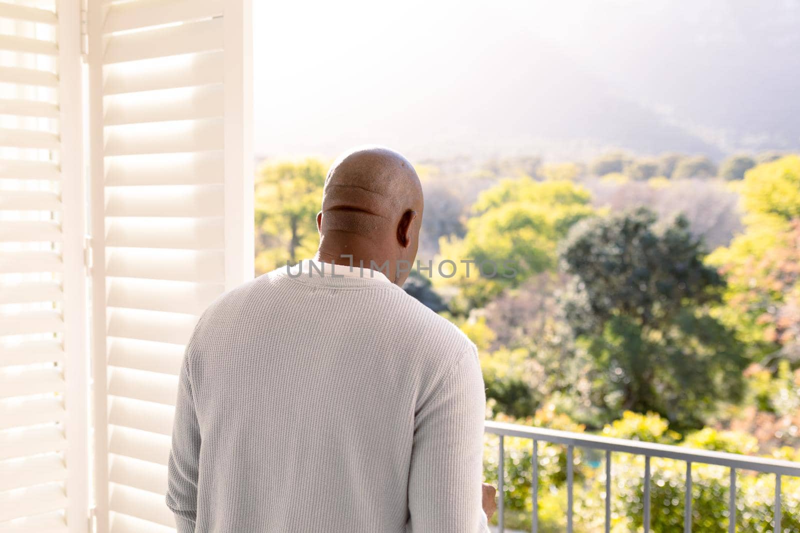 Back view of african american senior man standing on balcony and looking into distance. retirement lifestyle, spending time at home and garden.