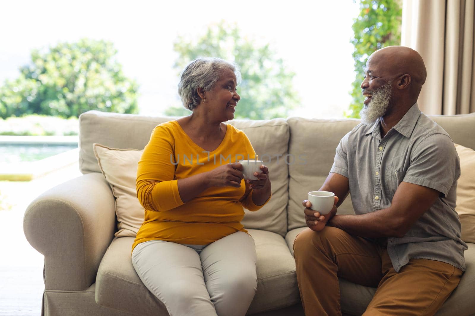 Senior african american couple sitting on sofa drinking coffee in living room. retreat, retirement and happy senior lifestyle concept.