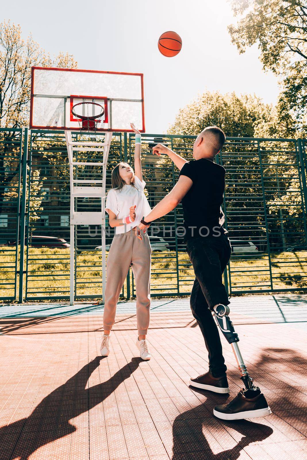 Young man with prosthetic leg playing basketball with his friend at a court.