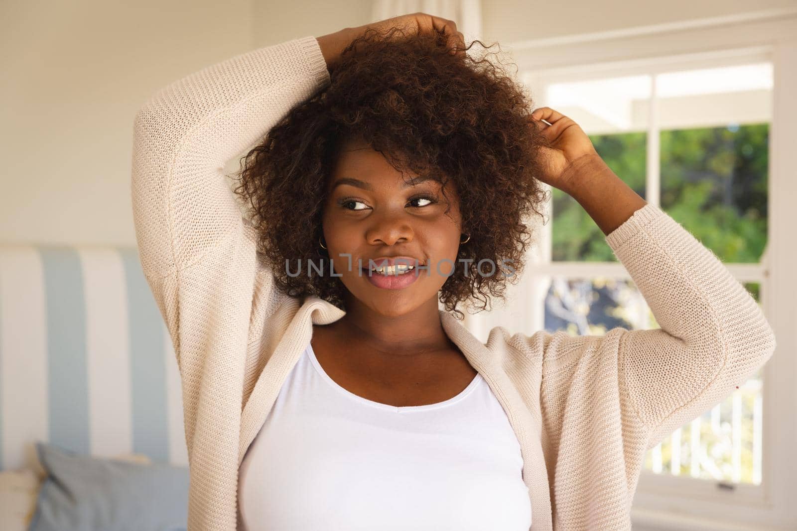Portrait of smiling african american woman touching her hair sitting on sofa at home. domestic lifestyle, enjoying leisure time at home.