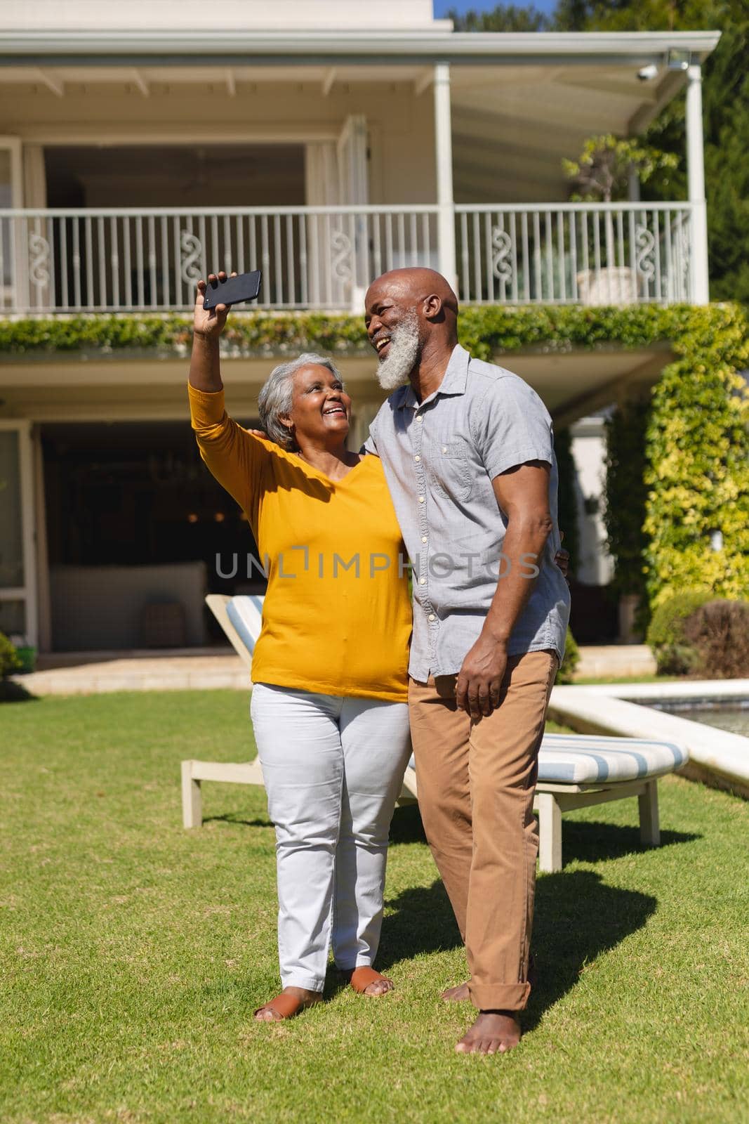 Senior african american couple spending time in sunny garden together taking selfies and smiling. retreat, retirement and happy senior lifestyle concept.