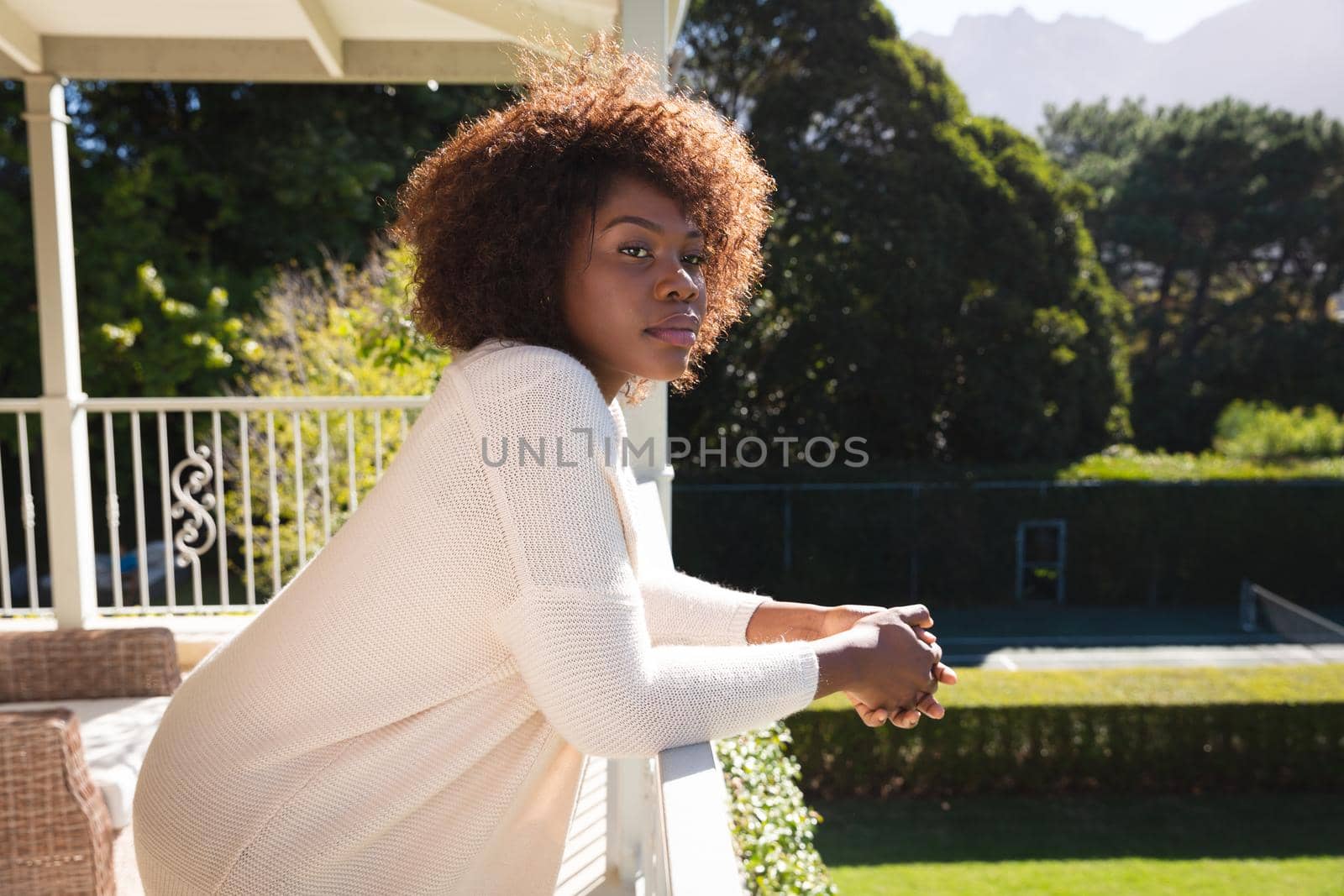 Happy african american woman relaxing on sunny balcony of country home enjoying the view. domestic lifestyle, enjoying leisure time at home.