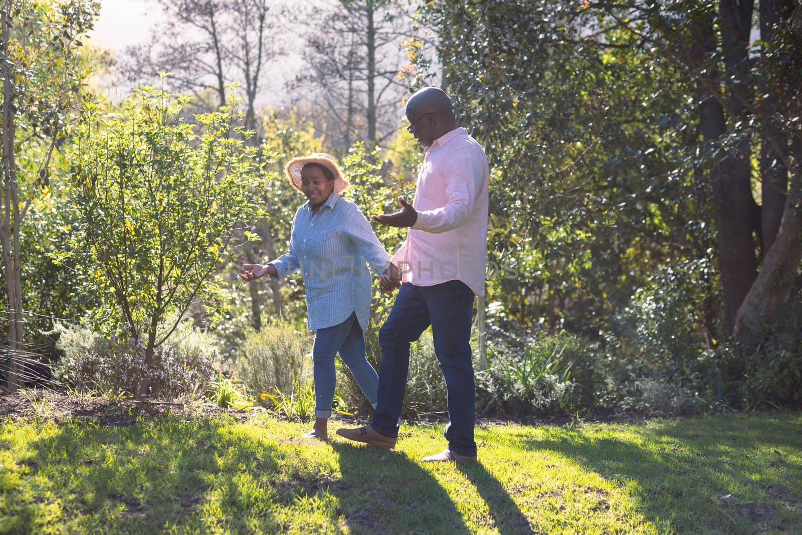 Happy african american senior couple walking, holding hands outdoors. retirement lifestyle, spending time at home and garden.