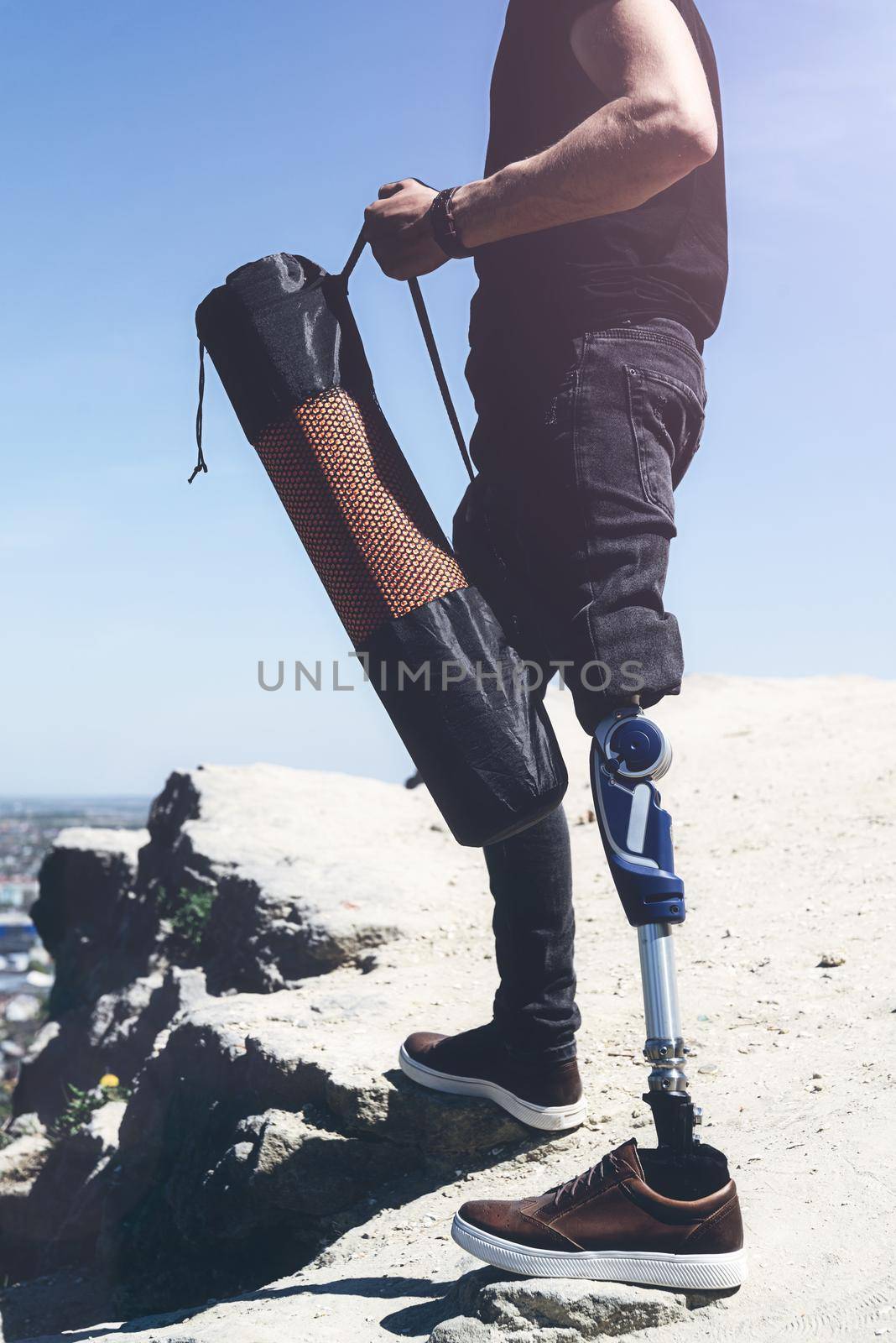 a man on a prosthetic leg travels the mountains. Dressed in black jeans and a T-shirt, he carrying mat.