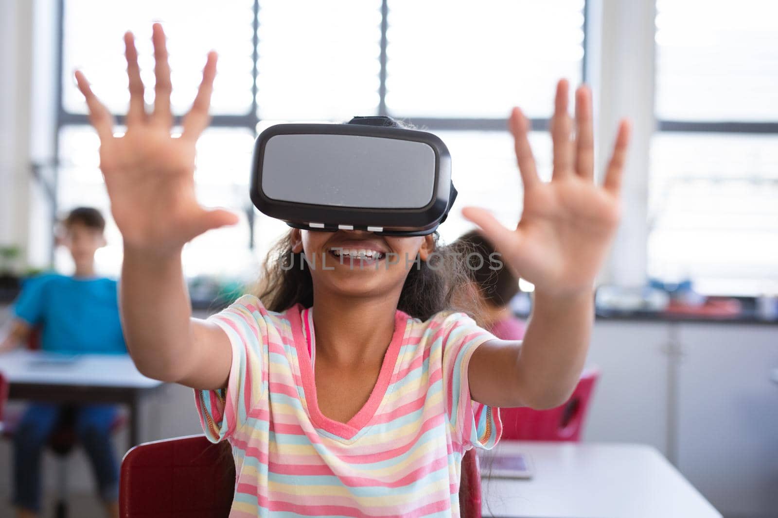 African american girl wearing vr headset gesturing while sitting on her desk in the class at school by Wavebreakmedia