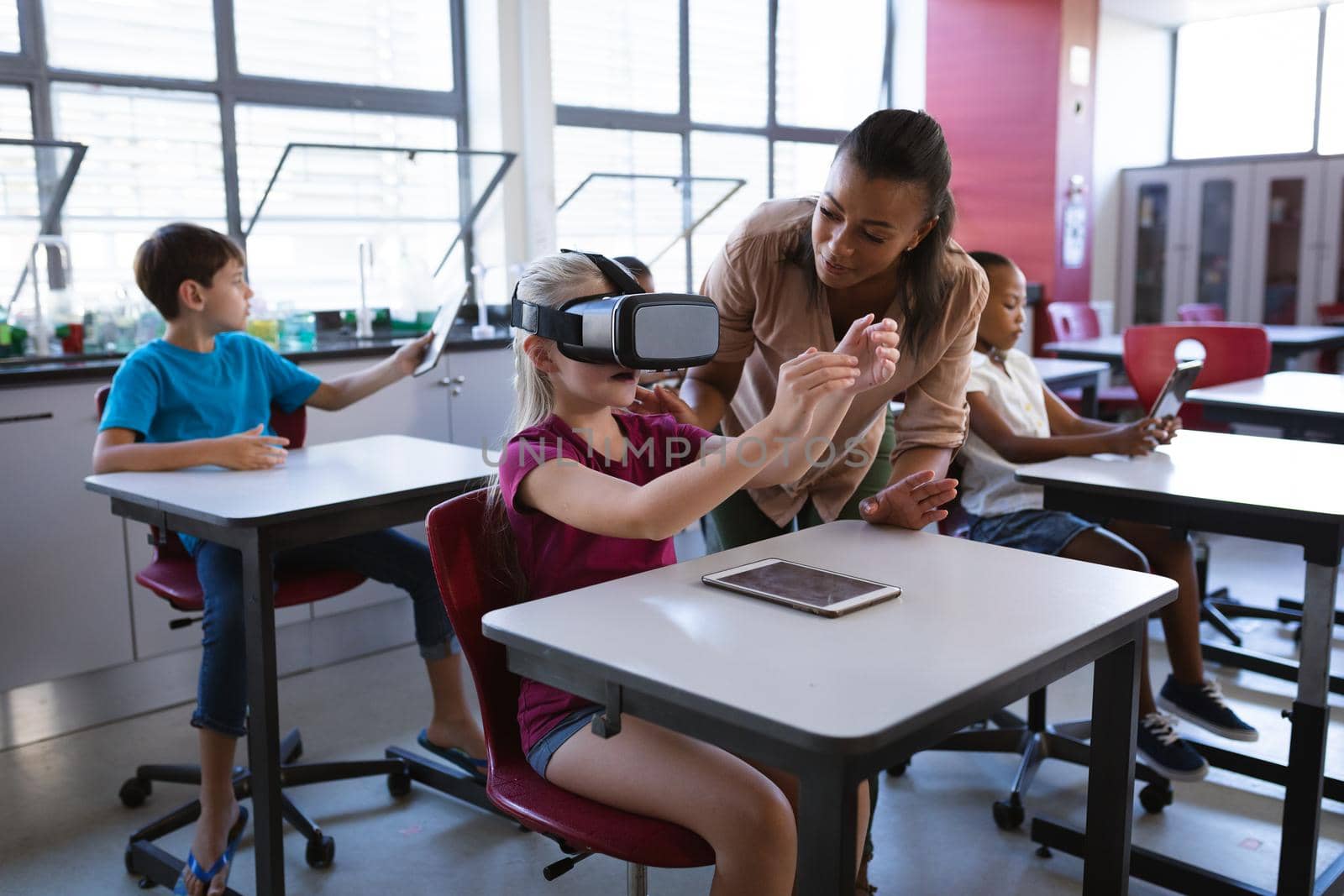 African american female teacher teaching caucasian girl to use vr headset in the class at school. school and education concept