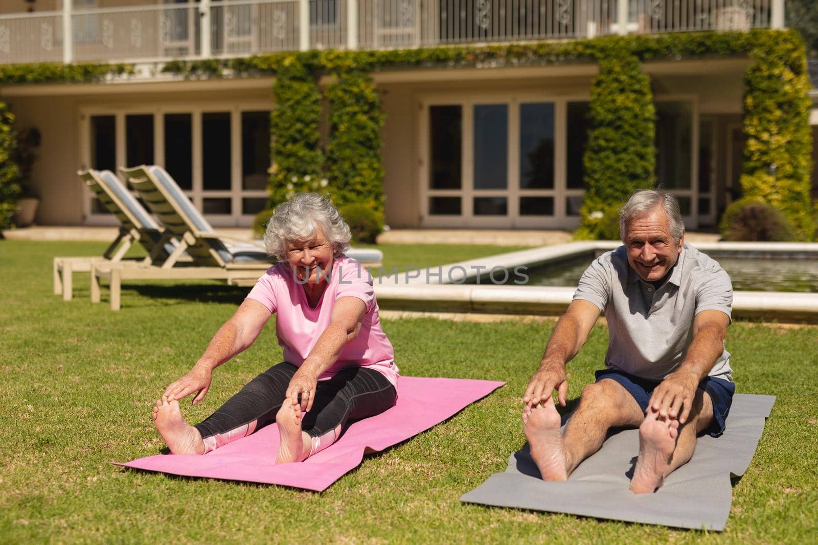 Portrait of senior caucasian couple practicing yoga, stretching in sunny garden. retirement retreat and active senior lifestyle concept.