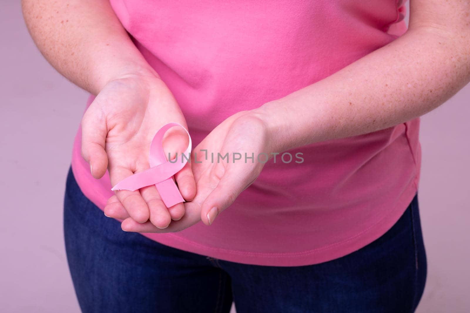 Hands of caucasian woman in pink tshirt holding pink ribbon. breast cancer positive awareness campaign concept digitally generated video.