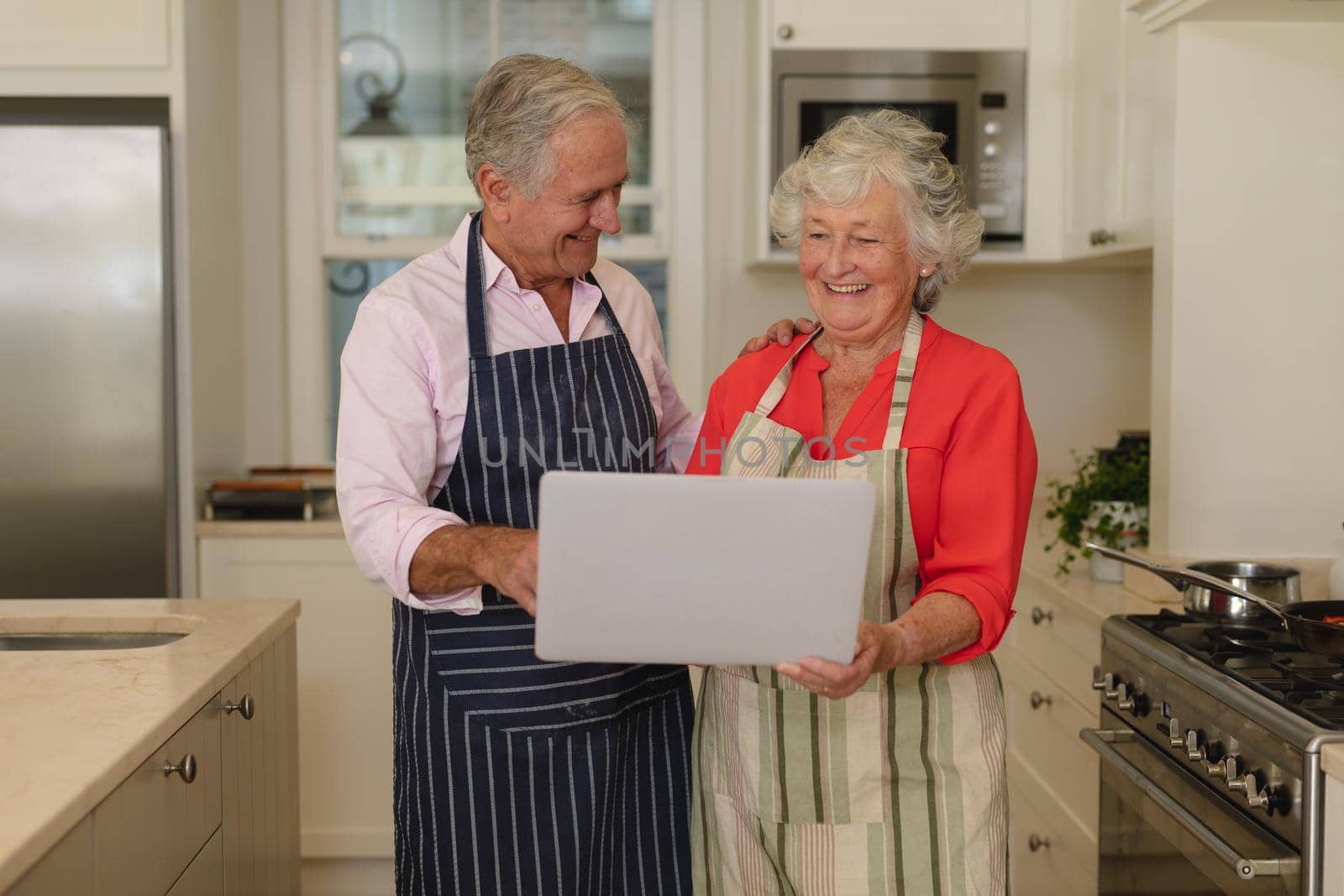 Senior caucasian couple using laptop together in kitchen. retreat, retirement and happy senior lifestyle concept.