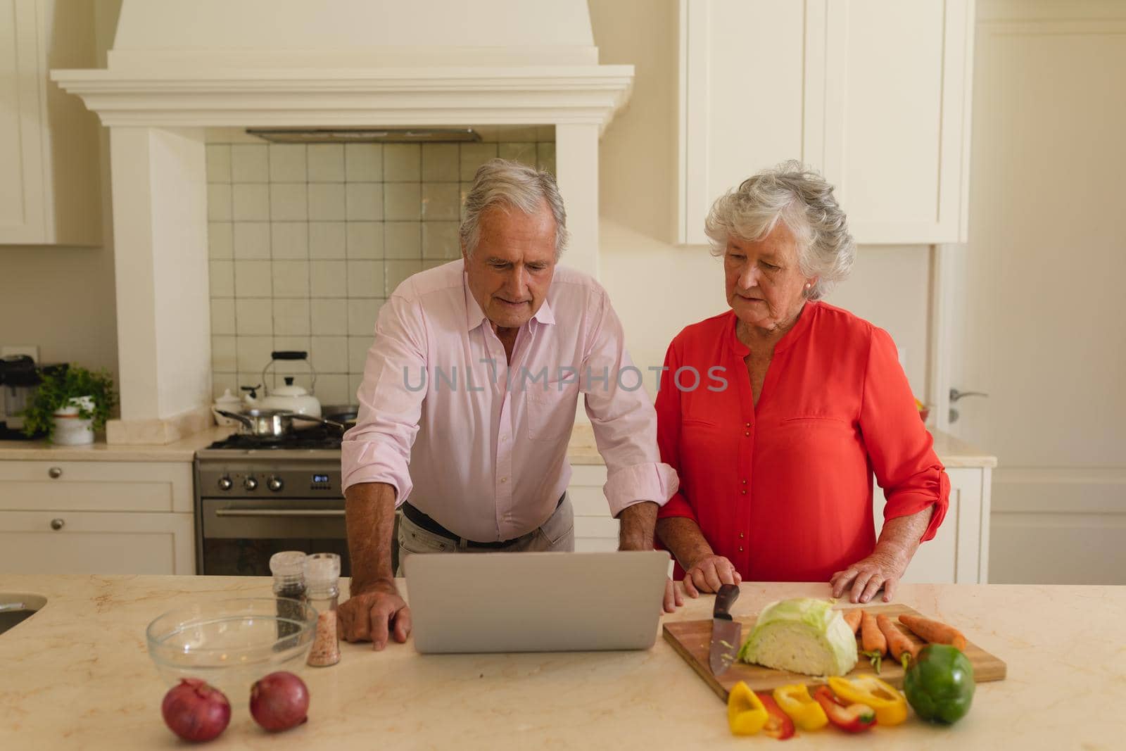 Senior caucasian couple cooking together and using laptop in kitchen. retreat, retirement and happy senior lifestyle concept.