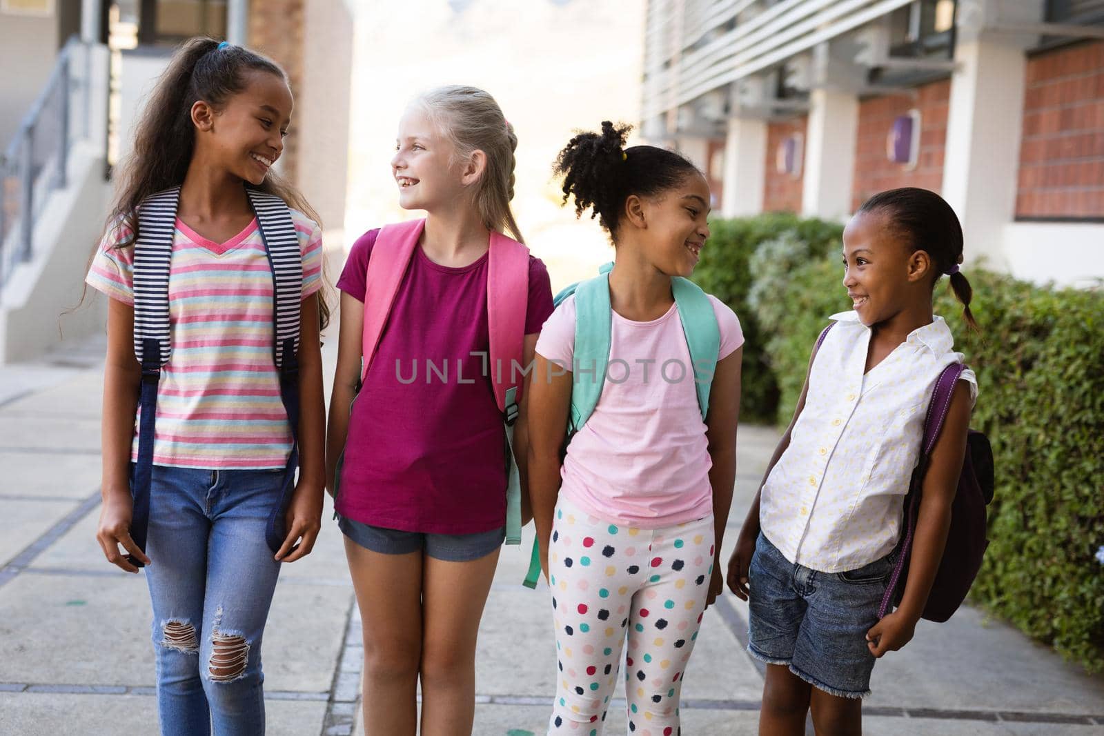 Group of diverse female students with backpacks smiling while looking at each other at school by Wavebreakmedia