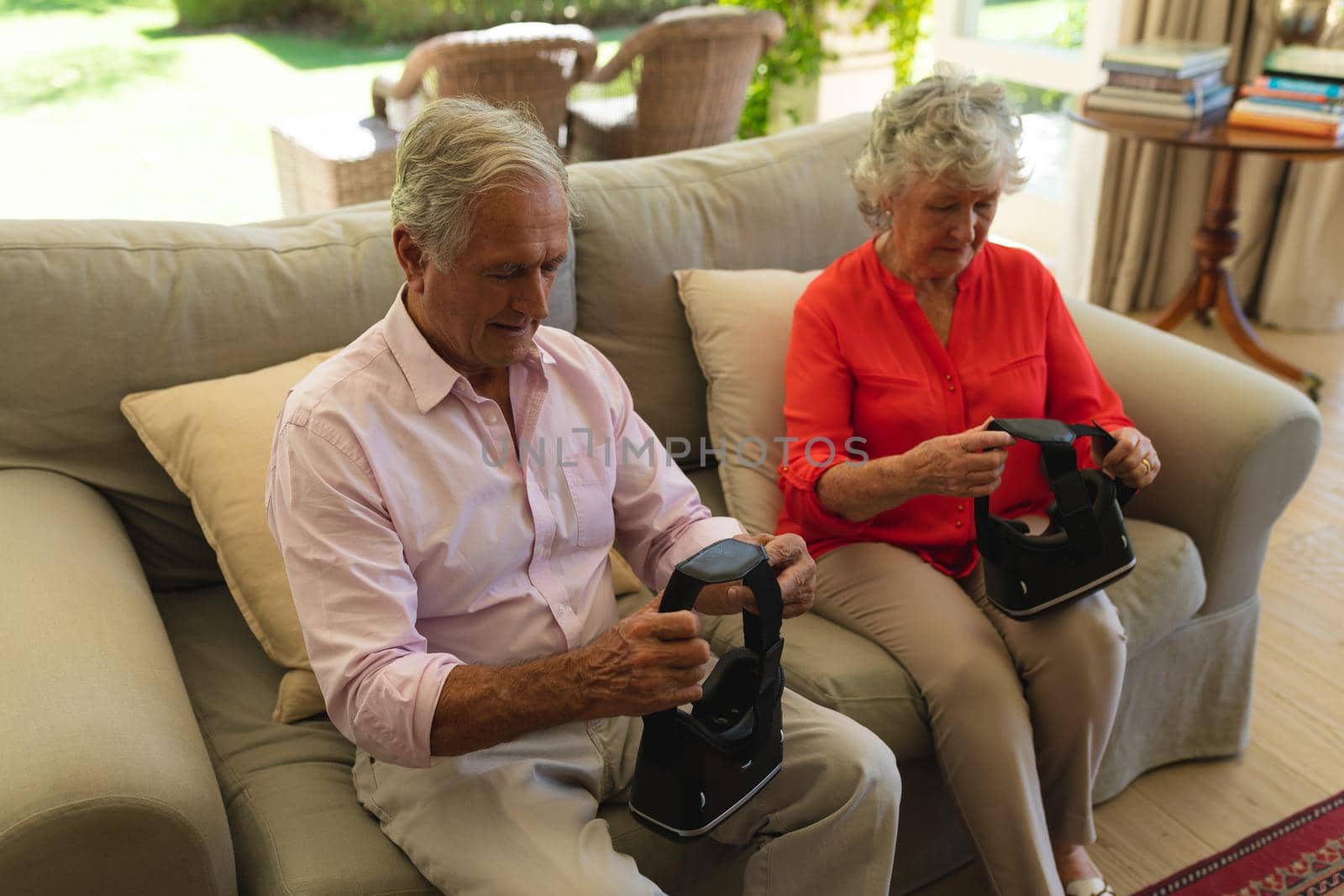Senior caucasian couple sitting on sofa together holding vr headset in living room by Wavebreakmedia