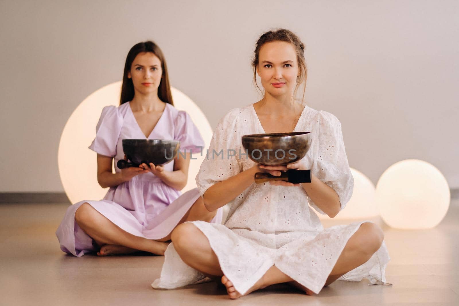 Two female yoga teachers playing a Tibetan bowl in the gym during a yoga retreat by Lobachad