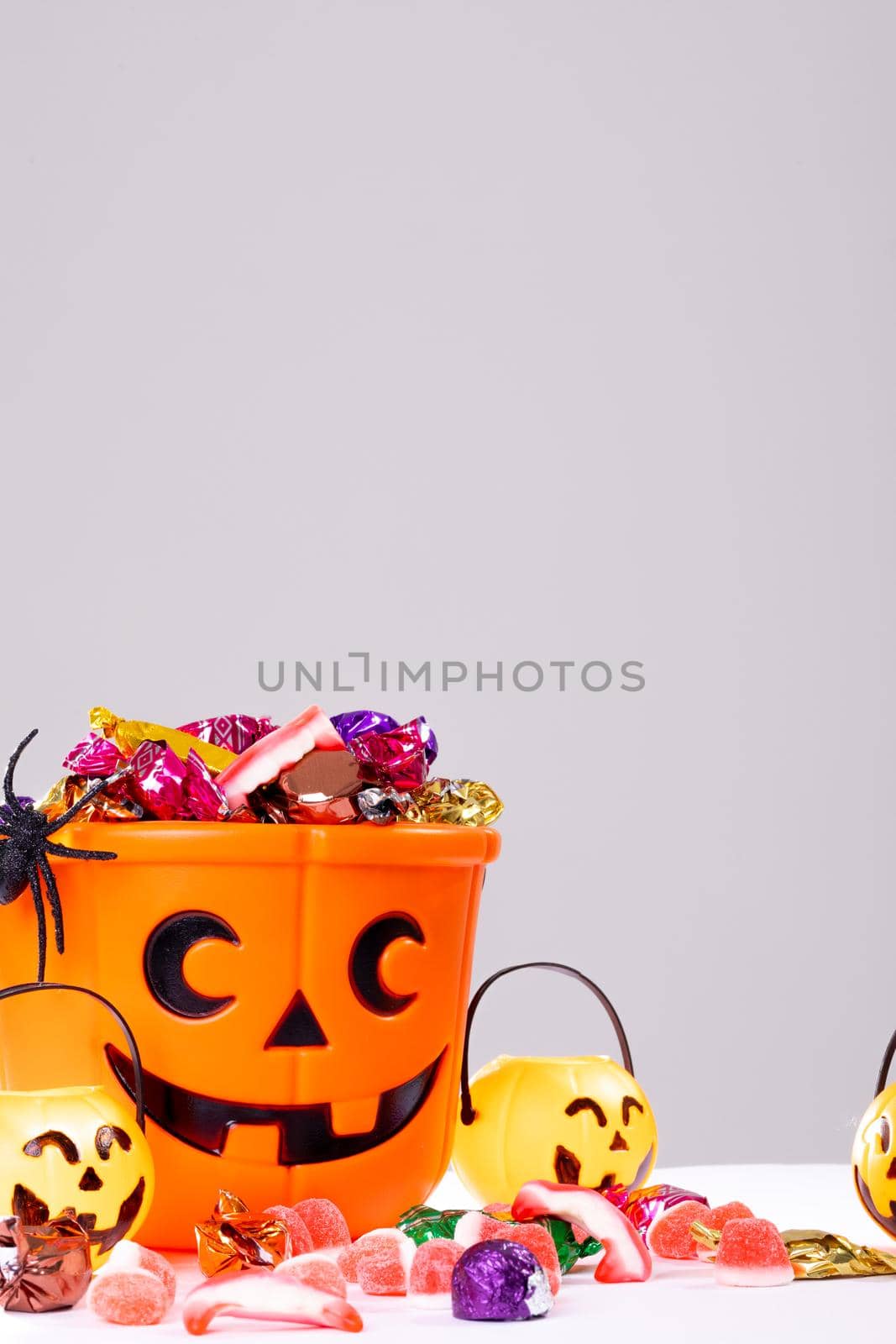Composition of halloween bucket with trick or treat sweets, spider and pumpkins on white background. halloween tradition and celebration concept.