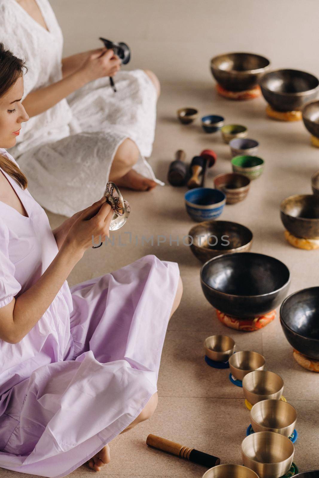 Two female yoga teachers play on Tibetan bowls in the gym during a yoga retreat by Lobachad