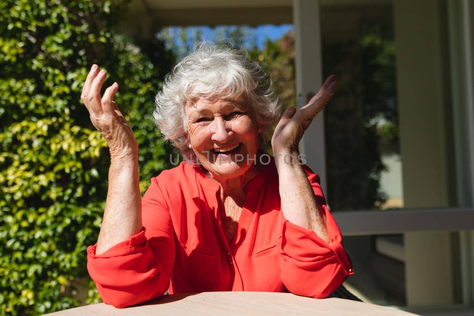 Portrait of senior caucasian woman sitting at table looking at camera and smiling in sunny garden. retreat, retirement and happy senior lifestyle concept.
