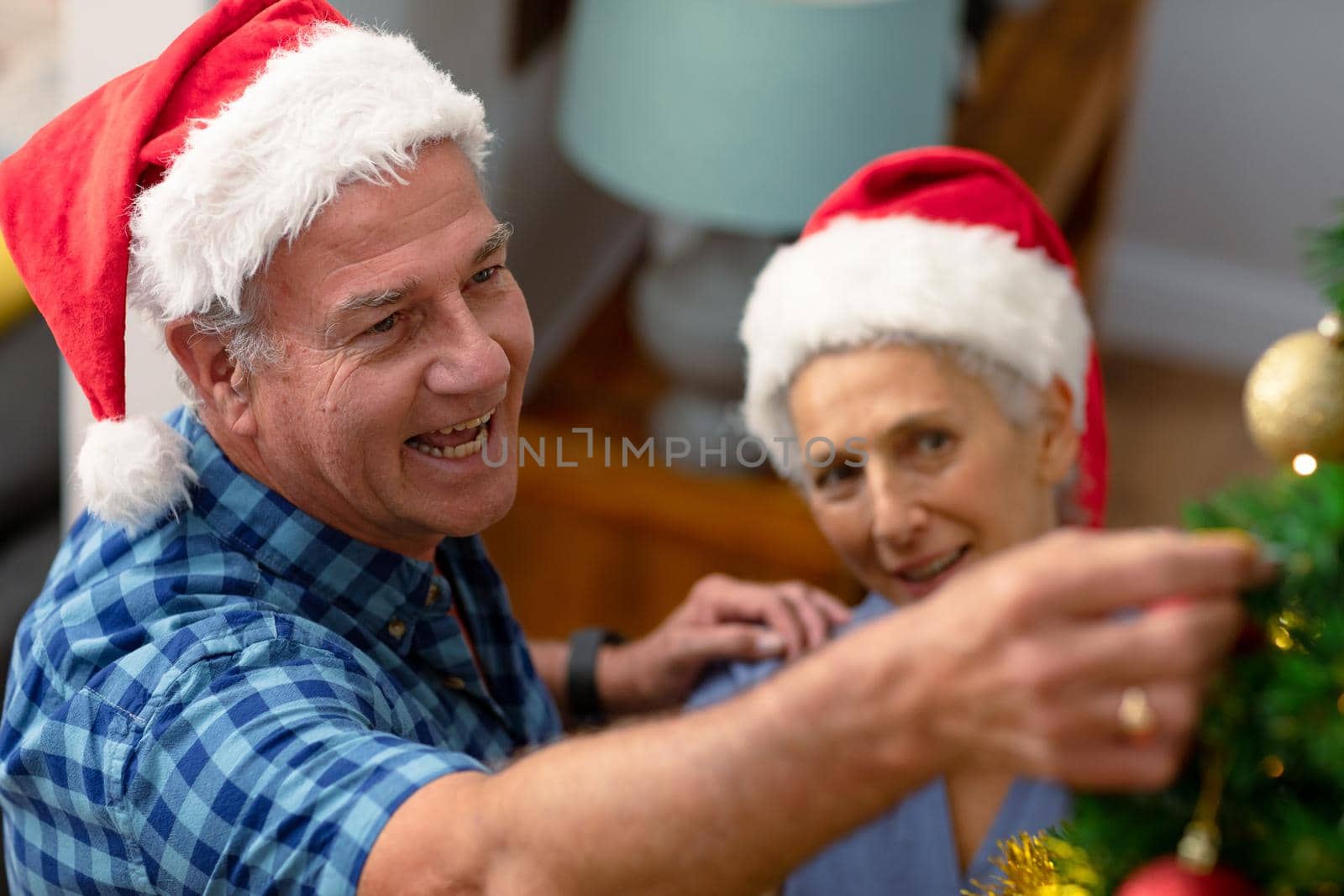 Happy caucasian senior couple wearing santa hat, decorating christmas tree. christmas, festivity and tradition at home.