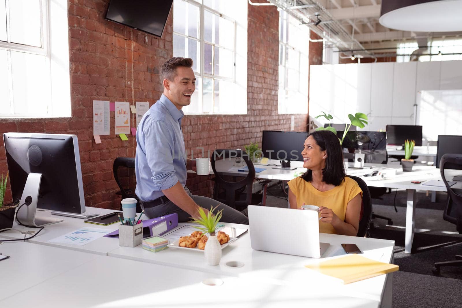 Caucasian male and female colleague sitting in office having coffee, talking and laughing. working in business at a modern office.