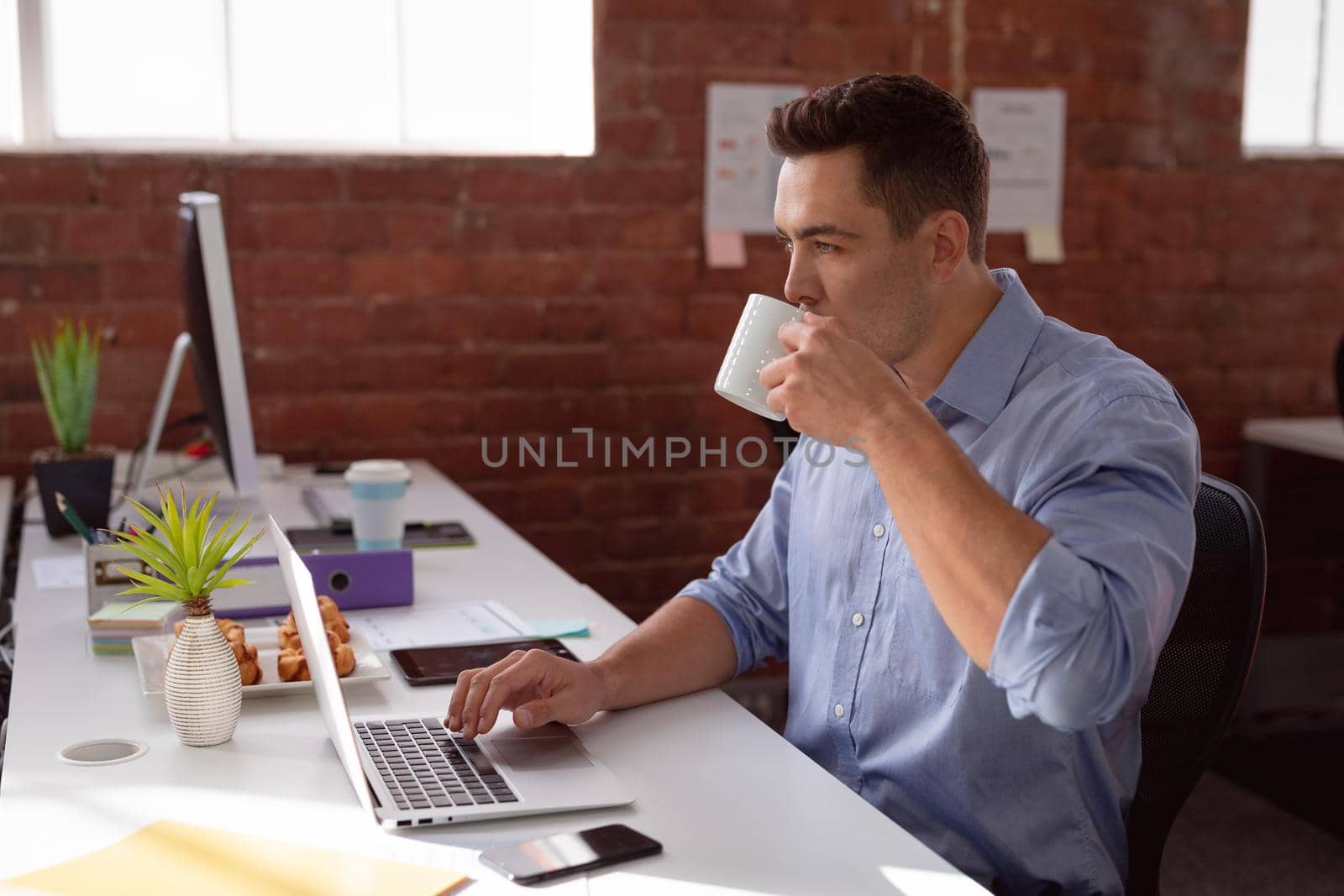Caucasian businessman sitting at desk in office using laptop and drinking coffee by Wavebreakmedia