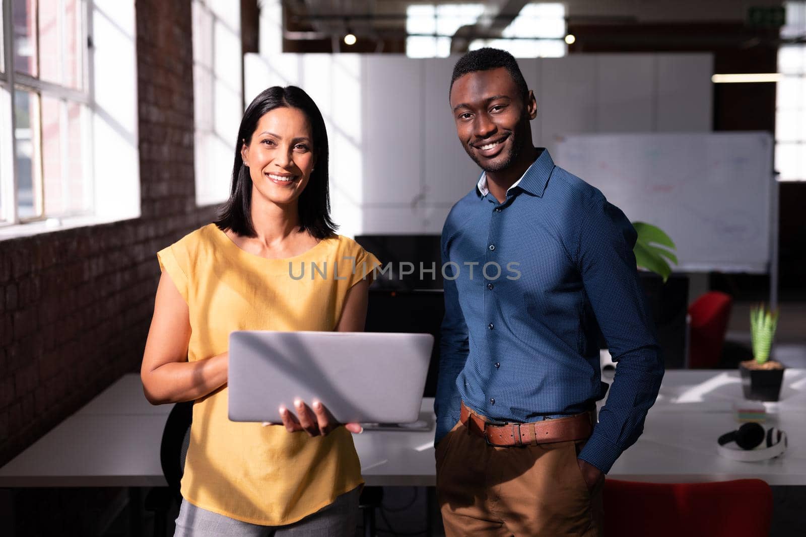 Portrait of smiling diverse male and female colleague standing in office looking at laptop together. working in business at a modern office.
