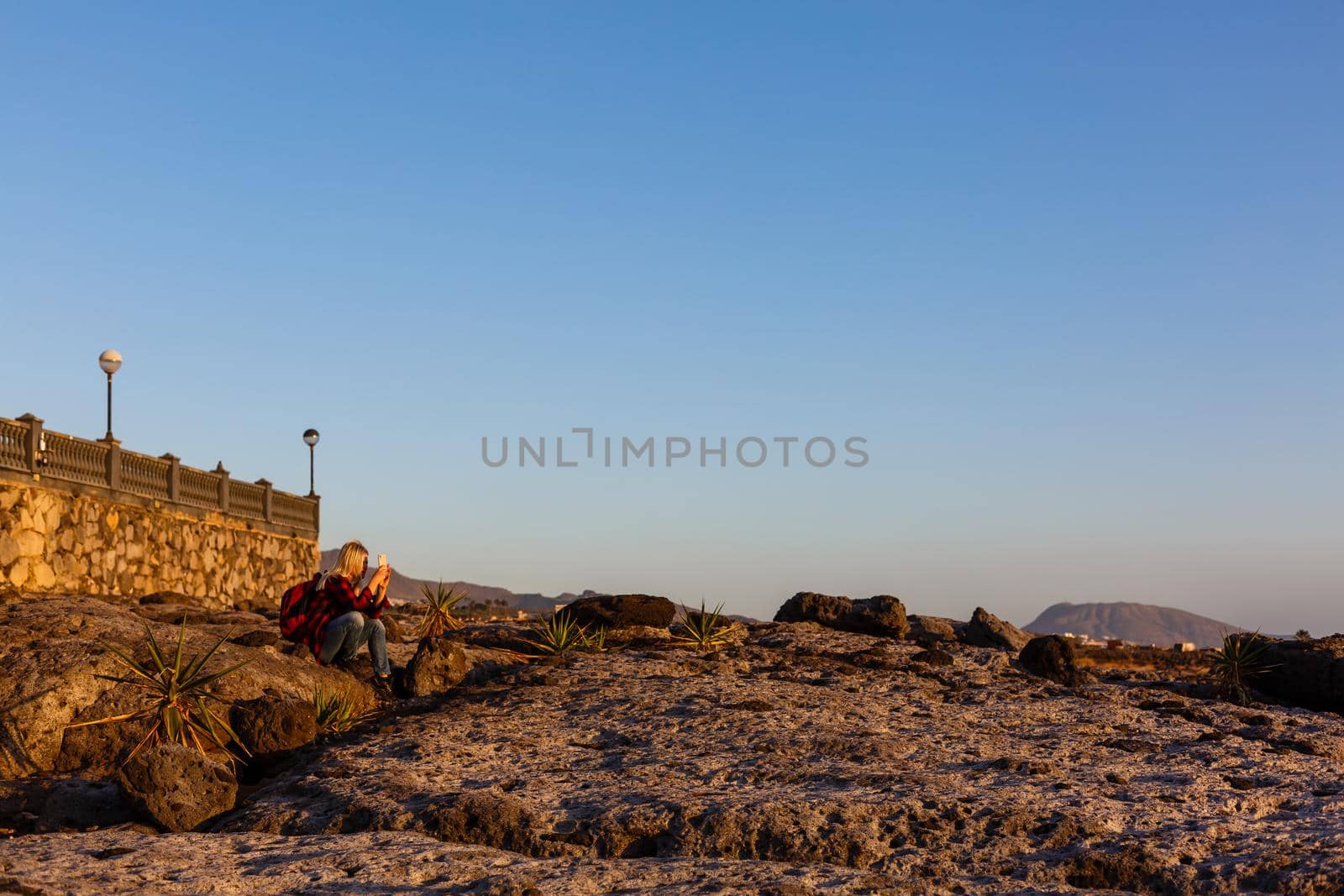 stylish woman alone sitting on stone coast and looking at sea by Andelov13