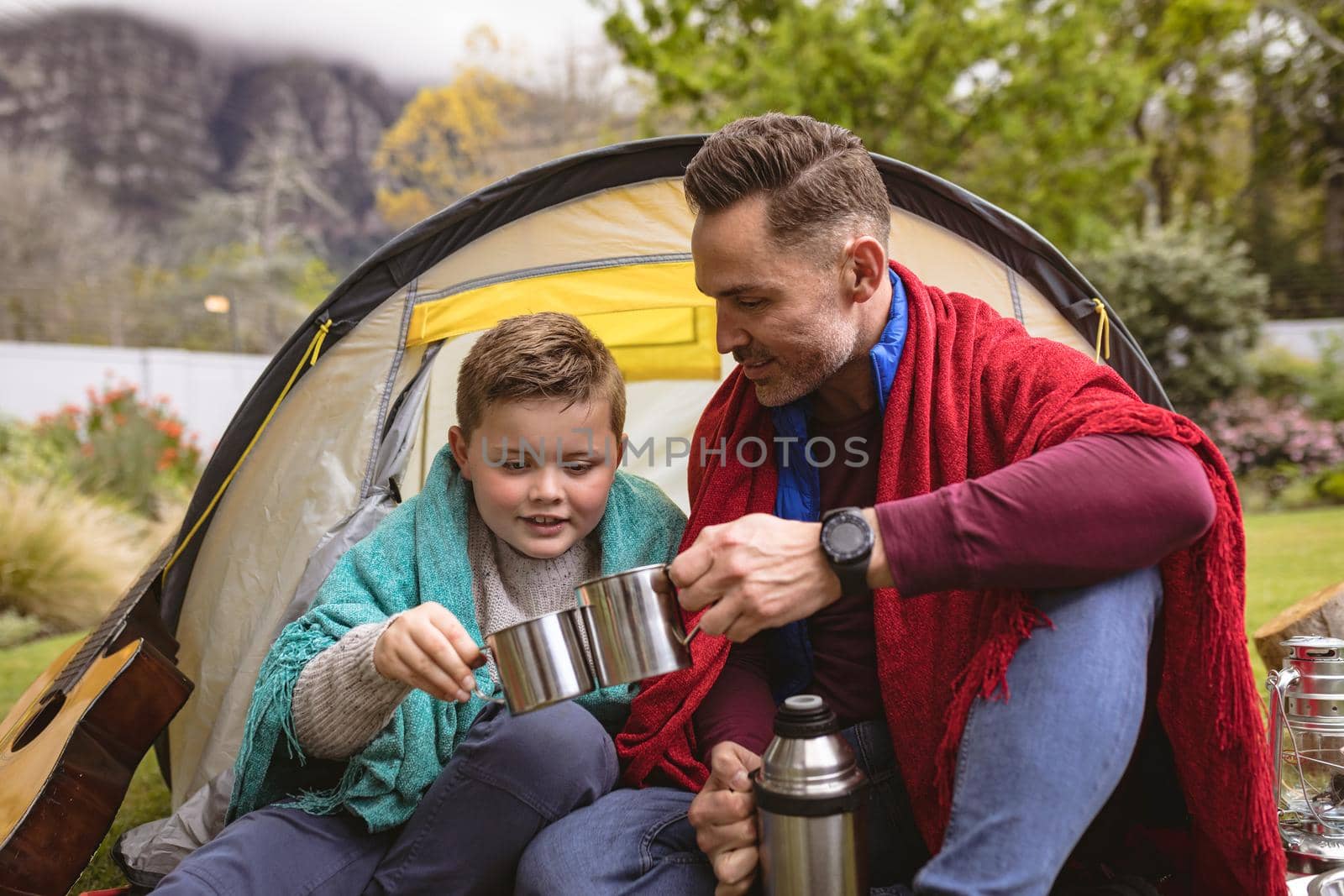 Caucasian father and son toasting their coffee cups while sitting in a tent in the garden. fatherhood and love concept