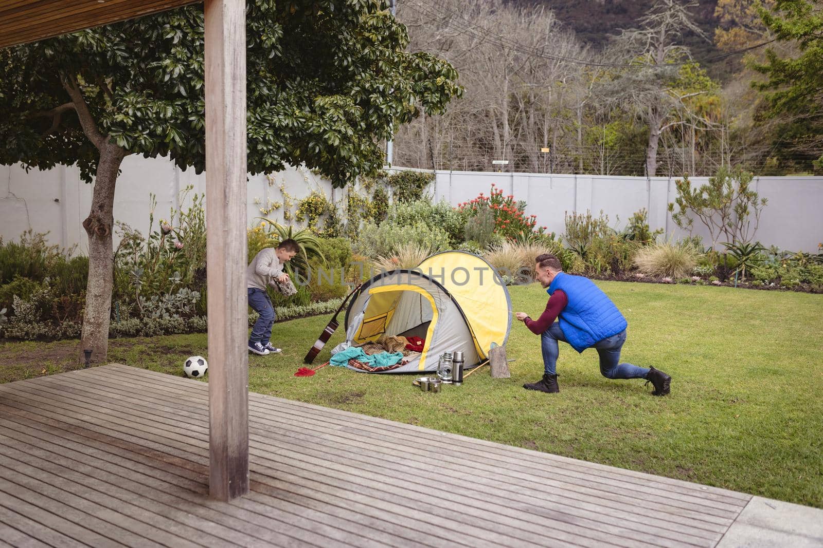 Caucasian father and son smiling while setting up a tent together in the garden. fatherhood and love concept