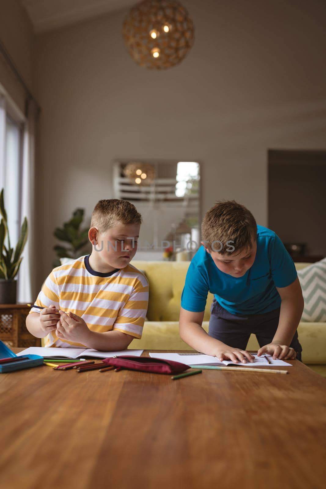 Two caucasian boys drawing in their books in the living room at home by Wavebreakmedia