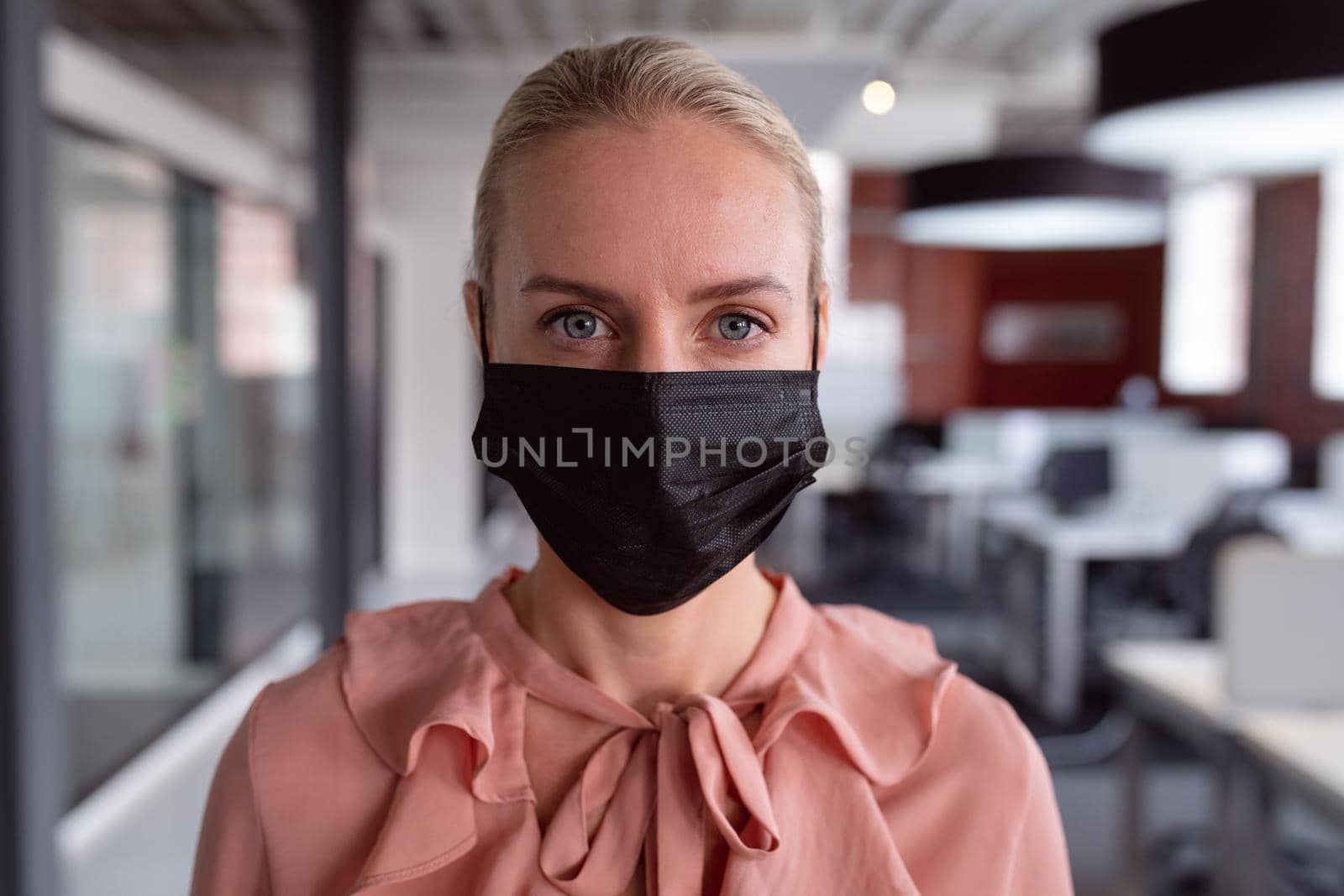 Portrait of caucasian businesswoman wearing face mask standing in office looking to camera. working in business at a modern office during coronavirus covid 19 pandemic.
