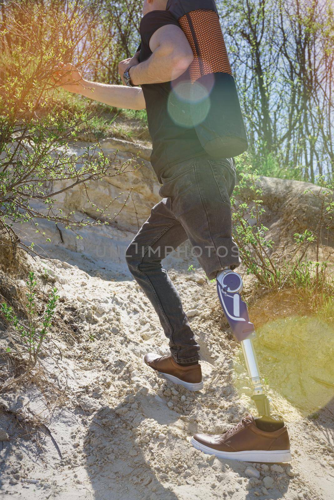 a man on a prosthetic leg travels the mountains. Dressed in black jeans and a T-shirt, he carrying mat.