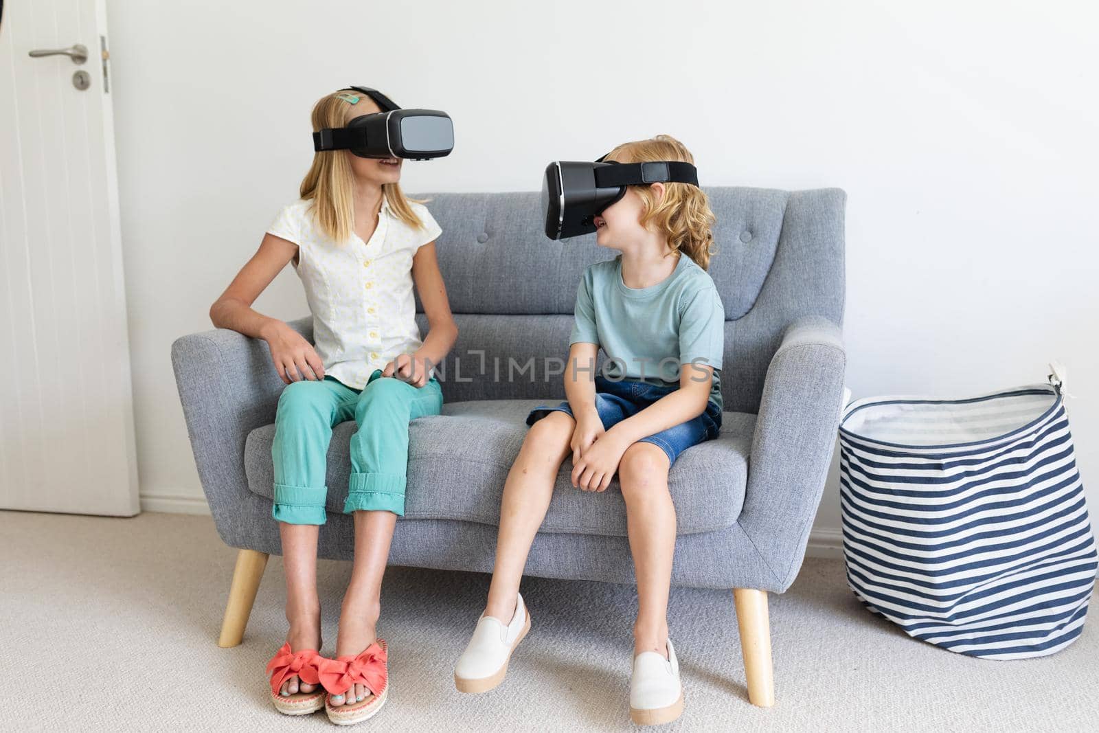 Caucasian brother and sister wearing vr headsets sitting on couch facing each other by Wavebreakmedia