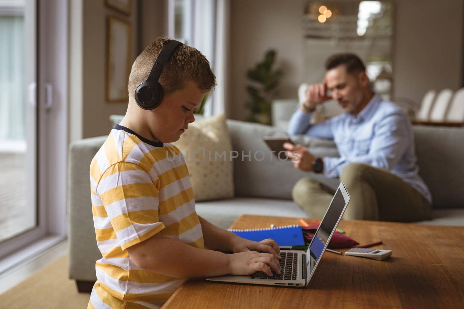 Caucasian boy wearing headphones using laptop in the living room at home. home schooling and education concept