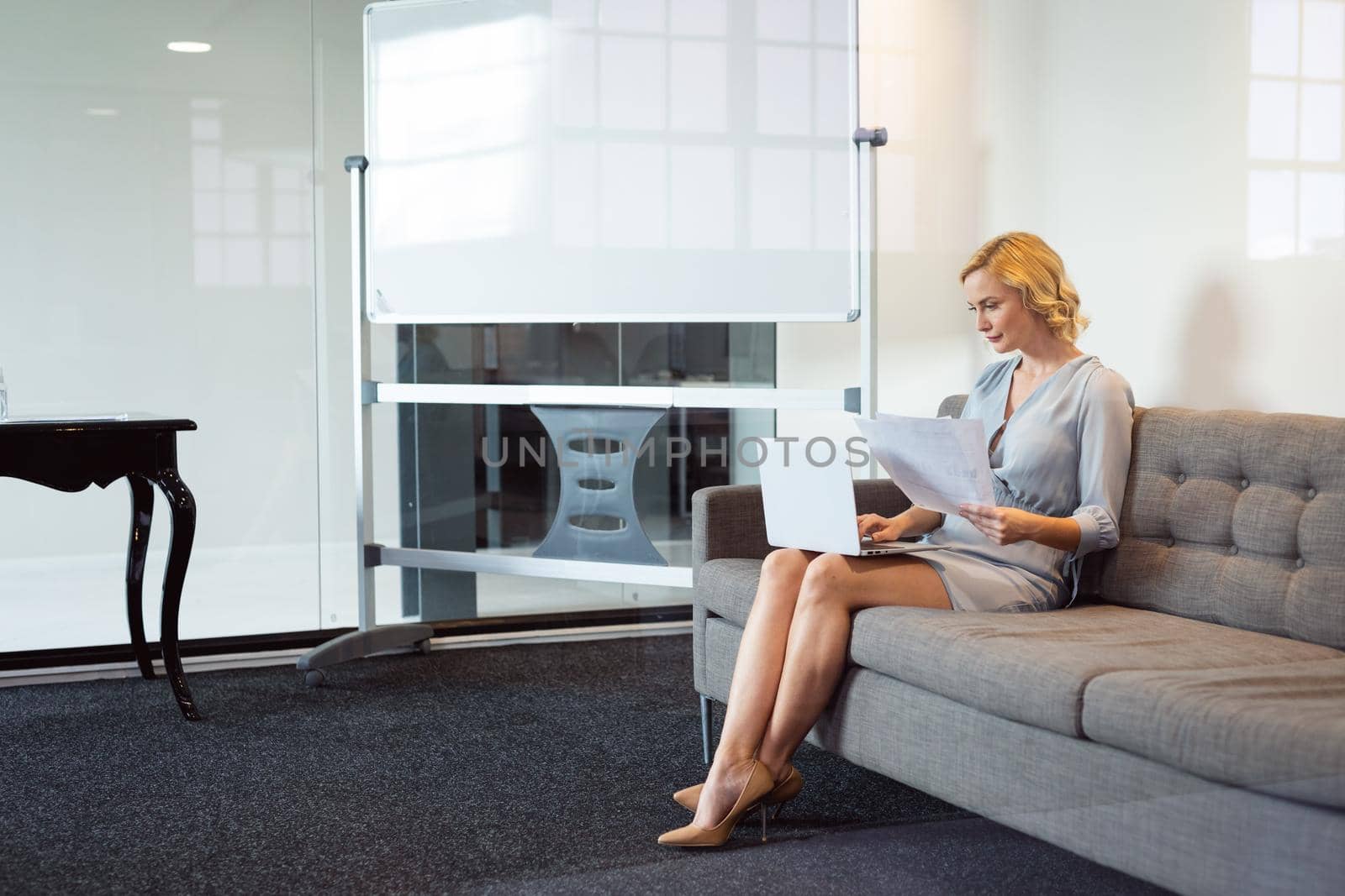 Caucasian businesswoman sitting in office lounge using laptop and holding paperwork. working in business at a modern office.