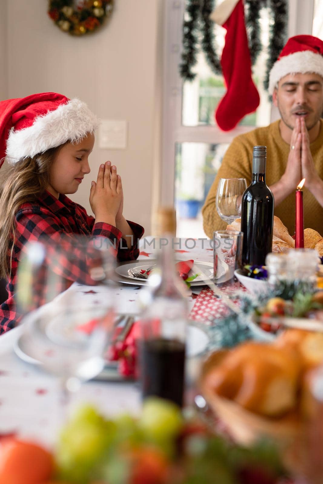 Caucasian daughter and father wearing santa hats praying at christmas table by Wavebreakmedia