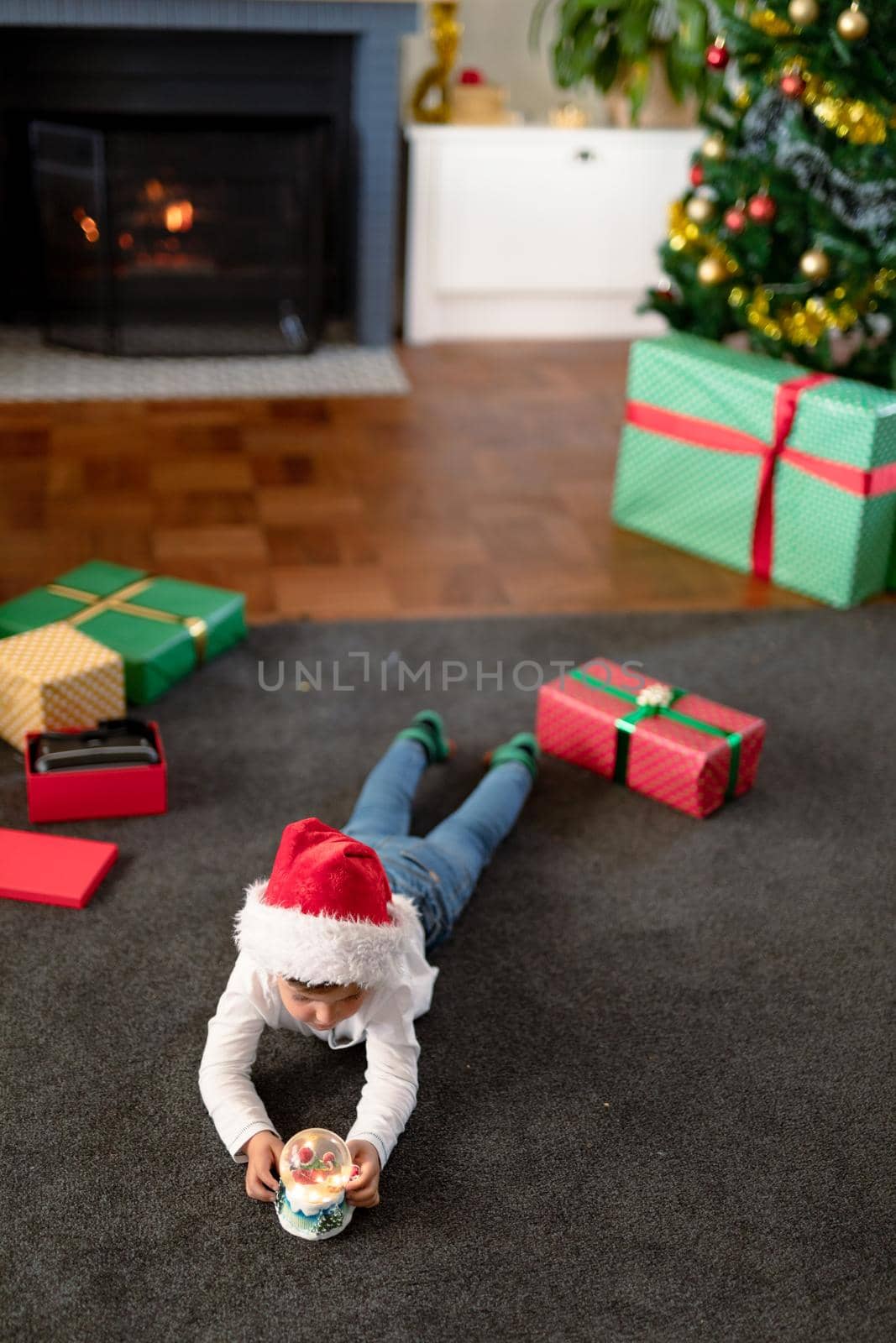 Focused caucasian boy wearing santa hat, looking at snow globe at christmas time. childhood, chiristmas, festivity and tradition at home.