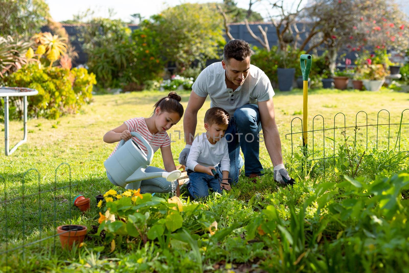 Happy caucasian father, daughter and son gardening and watering plants together. family time, having fun together at home and garden.