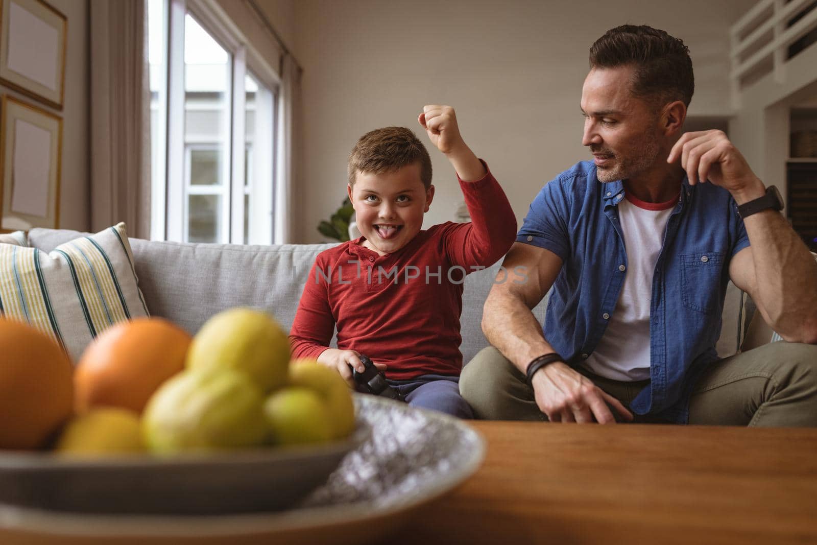 Caucasian boy celebrating while playing video games with his father sitting on the couch at home. gaming and entertainment concept