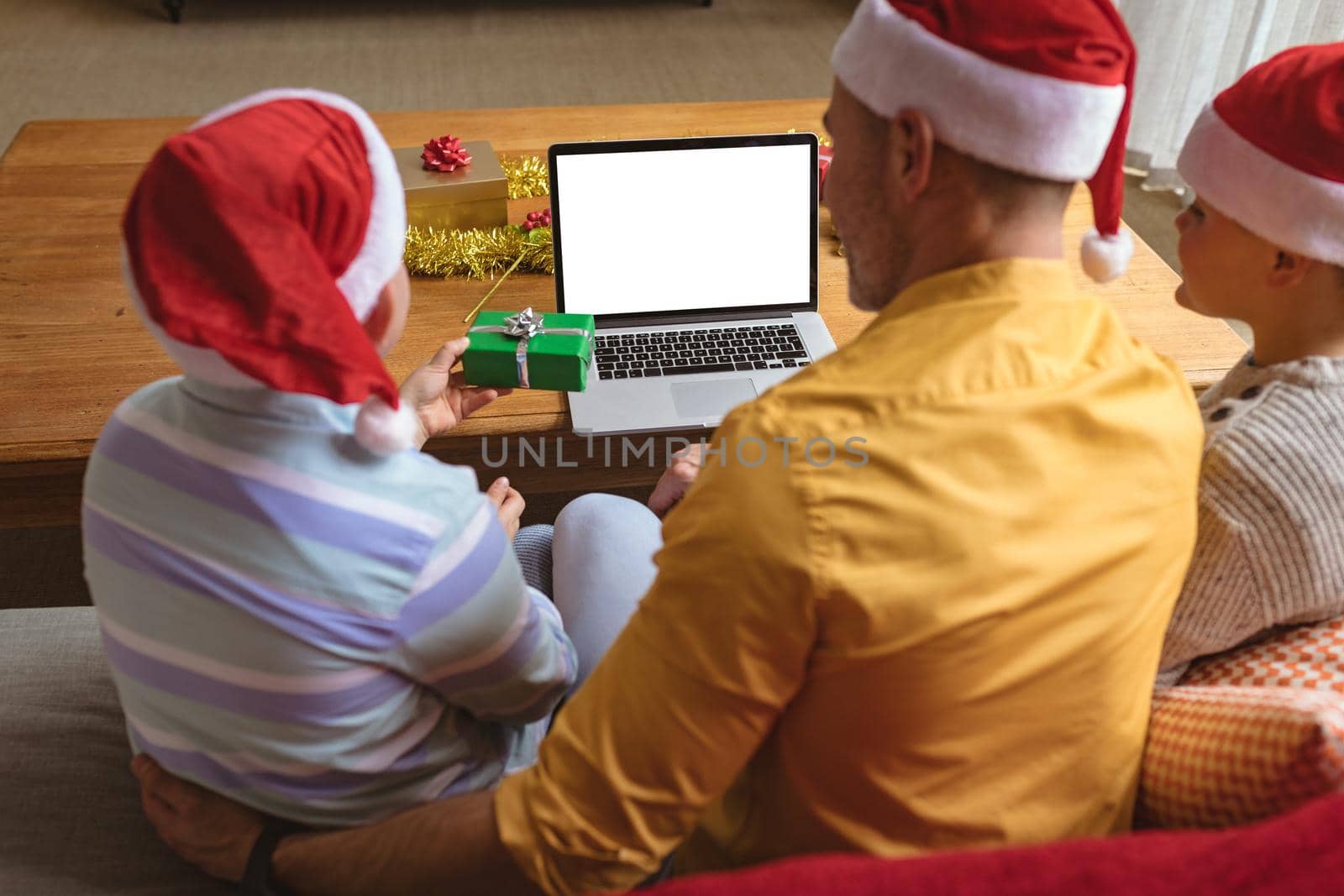 Caucasian father and two sons showing christmas gifts during video call on laptop with copy space. social distancing during covid 19 pandemic at christmas time