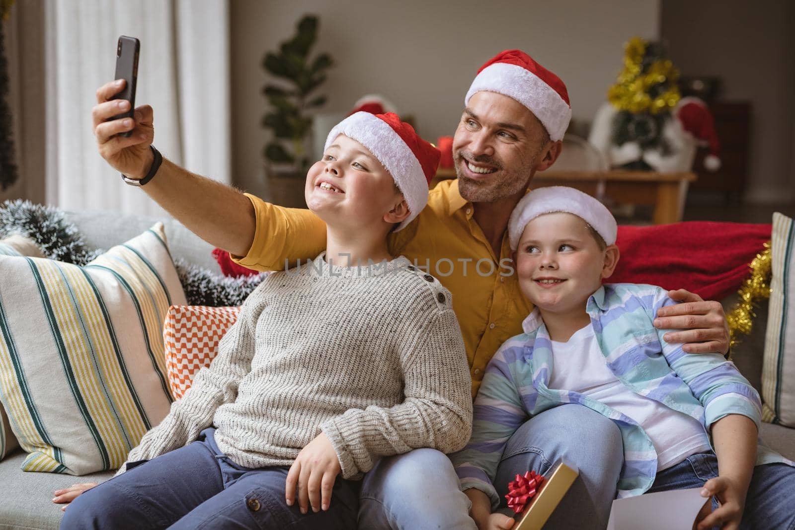 Caucasian father and two sons talking a selfie from smartphone at home during christmas. christmas festivity and celebration concept