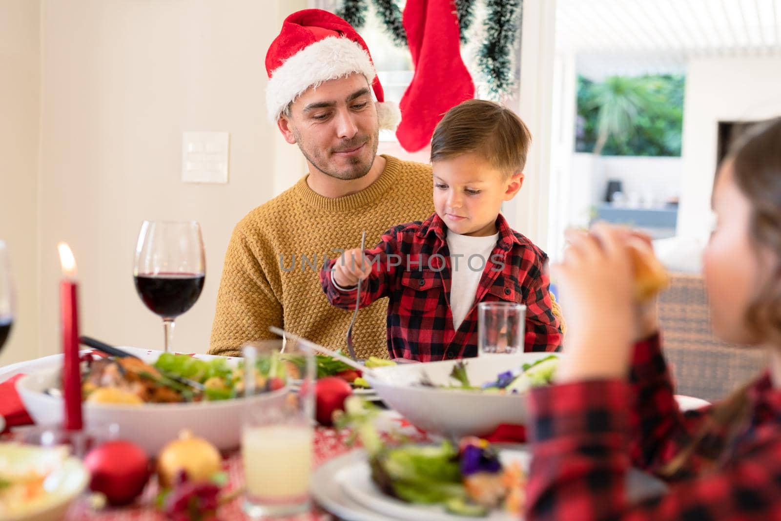 Happy caucasian father and son wearing santa hats sitting at christmas table by Wavebreakmedia