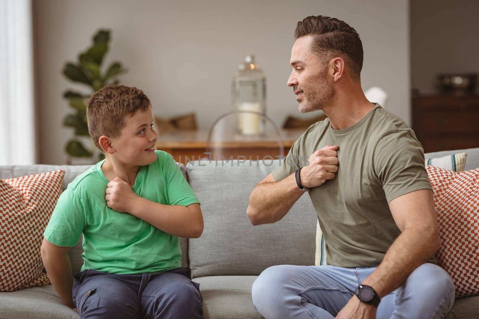 Caucasian father and son communicating using sign language while sitting on the couch at home. sign language learning concept