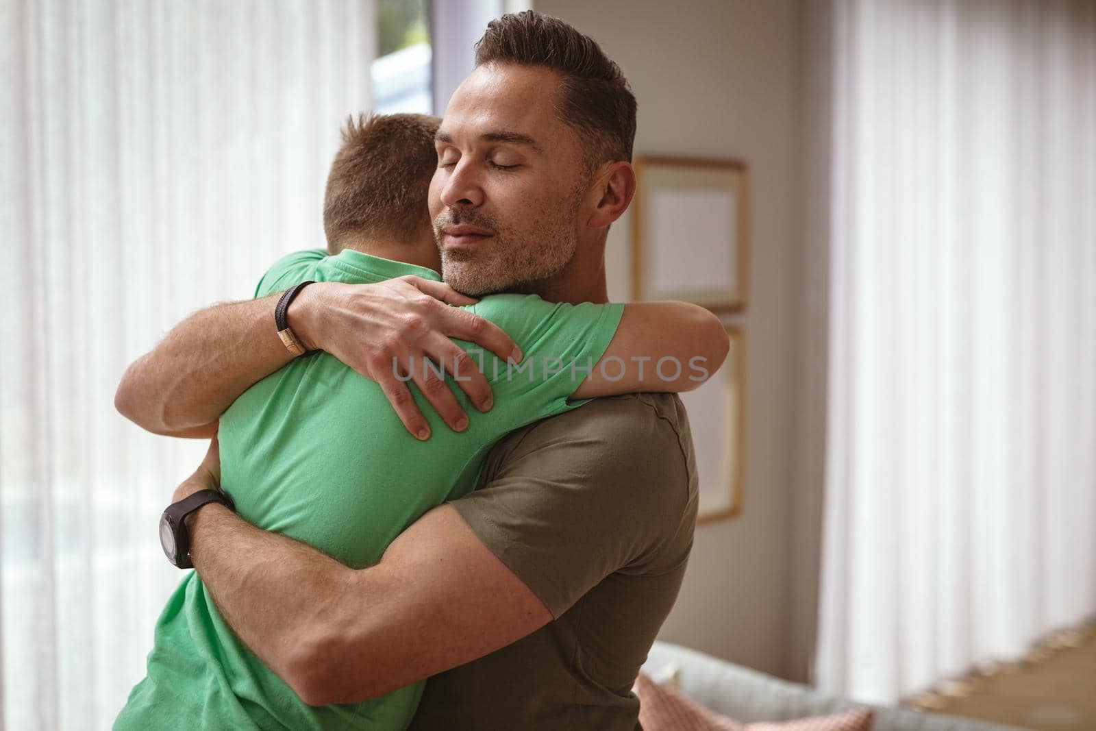 Caucasian father hugging his son in the living room at home. fatherhood and love concept
