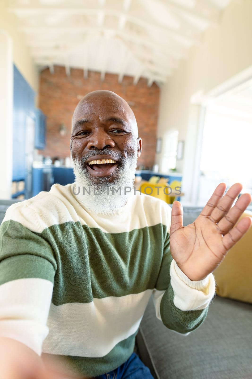 Happy senior african american man in living room sitting on sofa, making video call. retirement lifestyle, at home with technology.